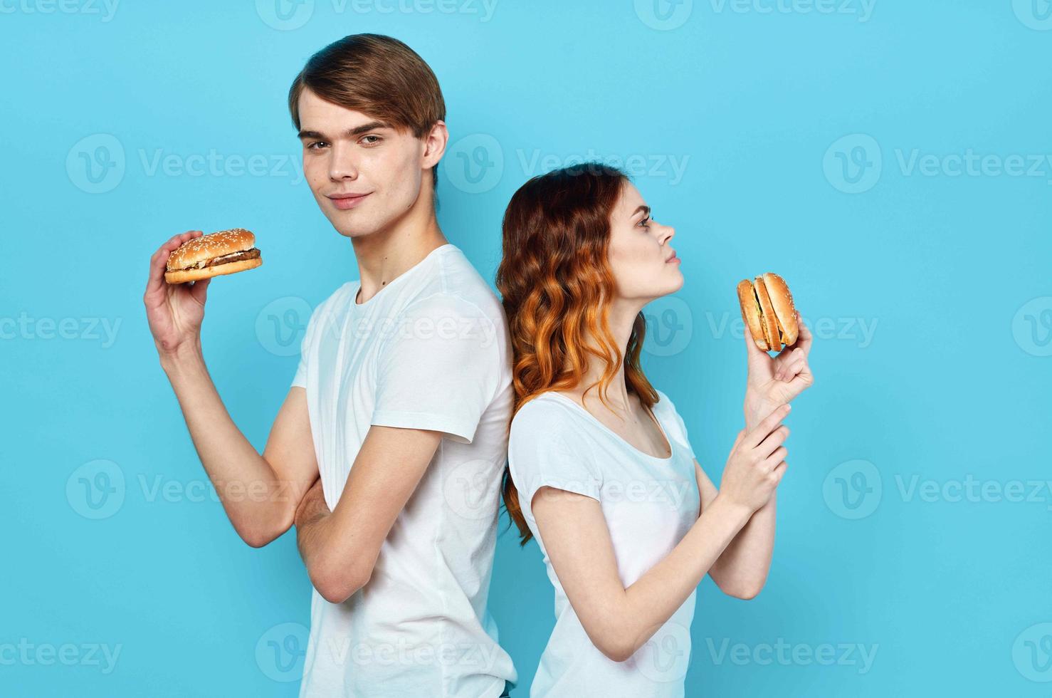 joven Pareja en blanco camisetas con hamburguesas en su manos rápido comida bocadillo foto