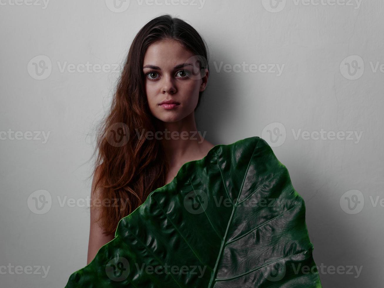 pretty red-haired woman with naked body covered with palm leaf light background photo