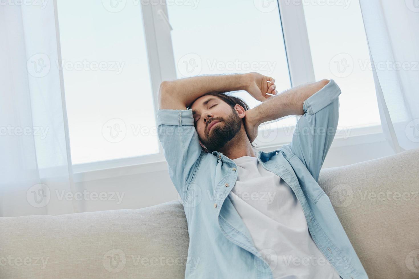 A man sits on the couch yawning and stretching after a nap, lack of sleep and fatigue from work and improper daily routine. photo