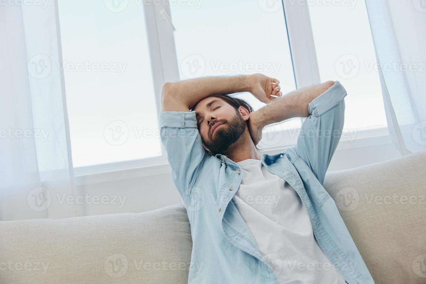 un hombre se sienta en el sofá bostezando y extensión después un siesta, carencia de dormir y fatiga desde trabajo y incorrecto diario rutina. foto