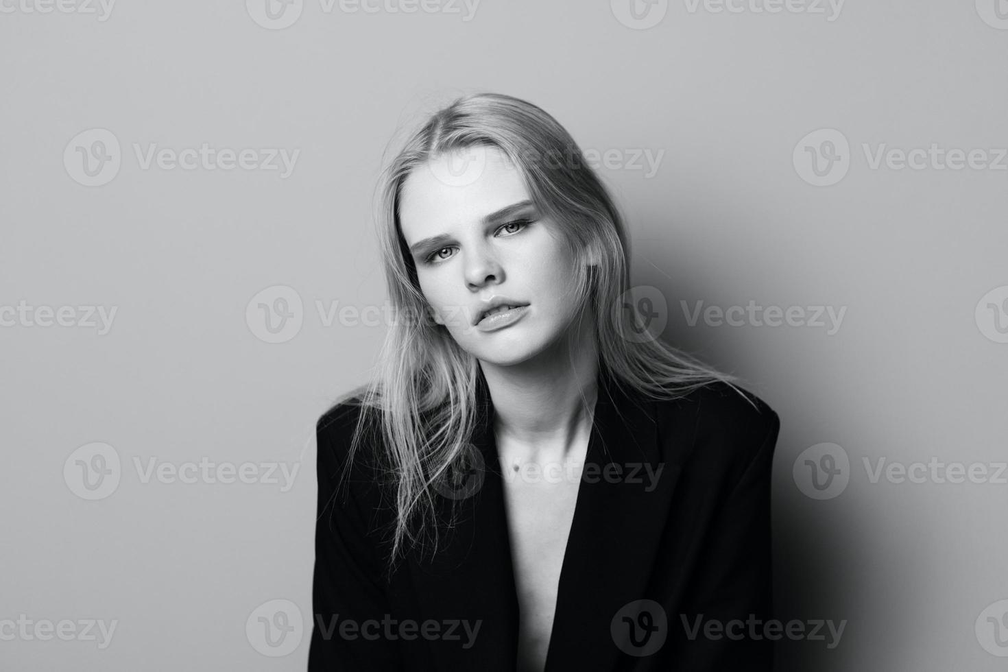 Young expressive beautiful blonde professional model posing isolated in studio dressing in black jacket looks at camera. Fashion Minimalistic concept photo