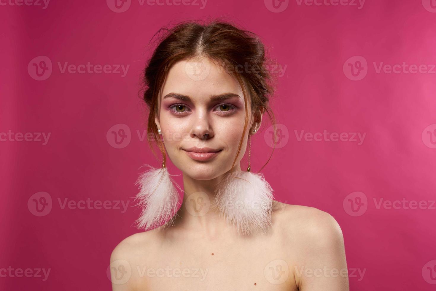 woman bare shoulders fluffy earrings bright makeup pink background photo