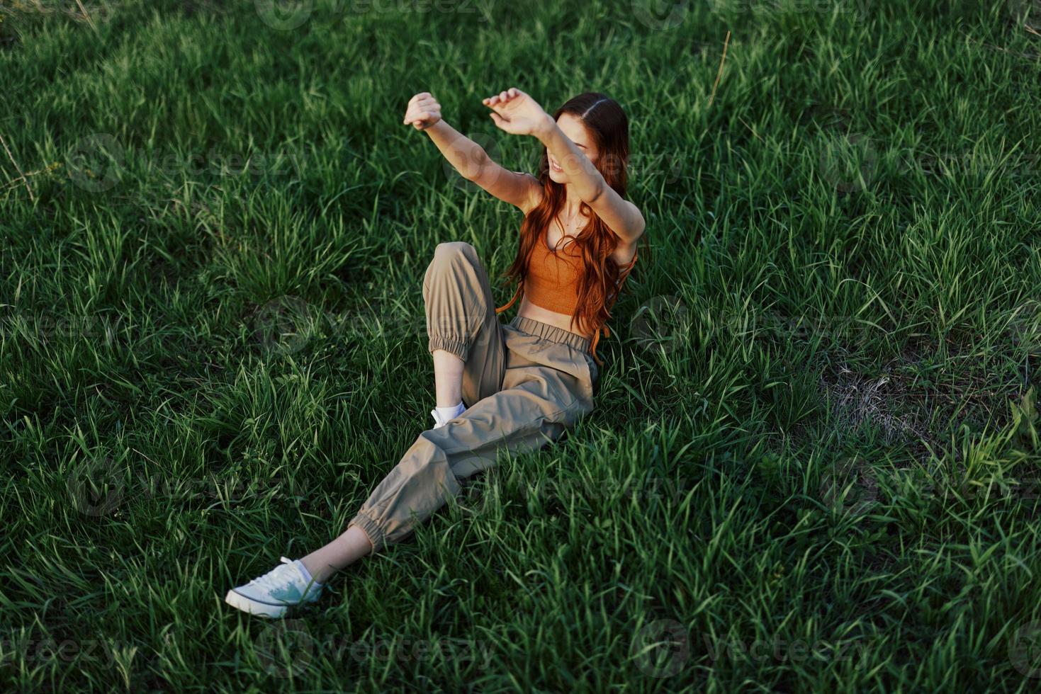 un mujer relajante en el césped en el parque, vistiendo pantalones y un parte superior y acecho el puesta de sol. el concepto de relajante sin el teléfono y el Internet en armonía con uno mismo en el Fresco aire foto