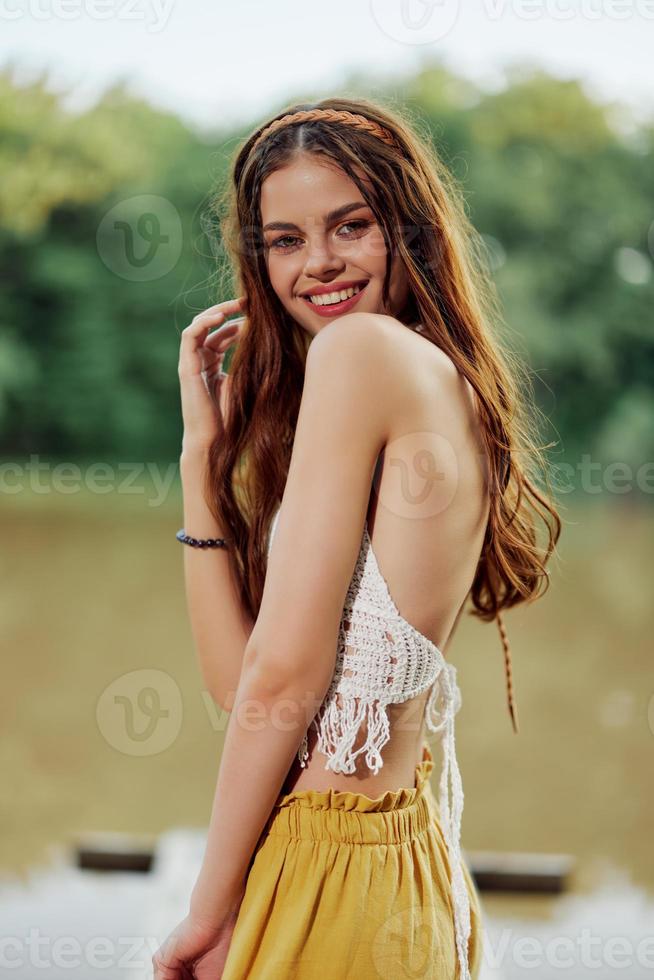 A young woman smiling in an image of a hippie and eco-dress dancing in nature by the lake wearing a hat and yellow pants in the summer sunset photo