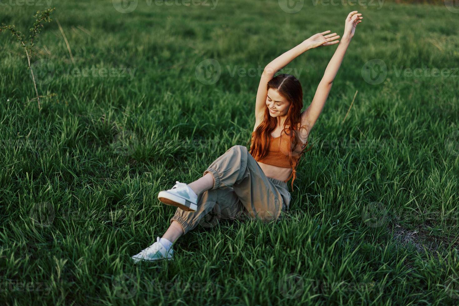 A woman lies on the green grass in the park with her legs up and having fun against the lawn, viewed from above. The concept of relaxing in nature and caring for the environment photo