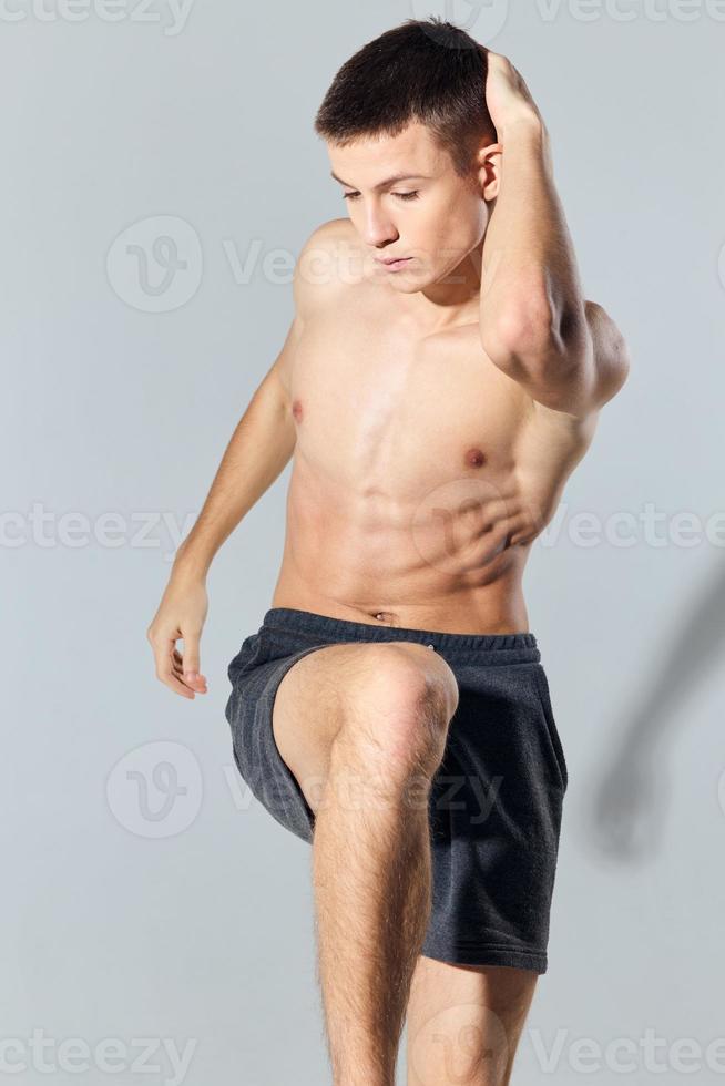 sport man in shorts doing exercise leaning forward on gray background photo