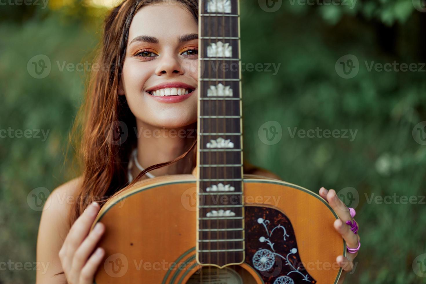 joven hippie mujer con eco imagen sonriente y mirando dentro el cámara con guitarra en mano en naturaleza en un viaje foto