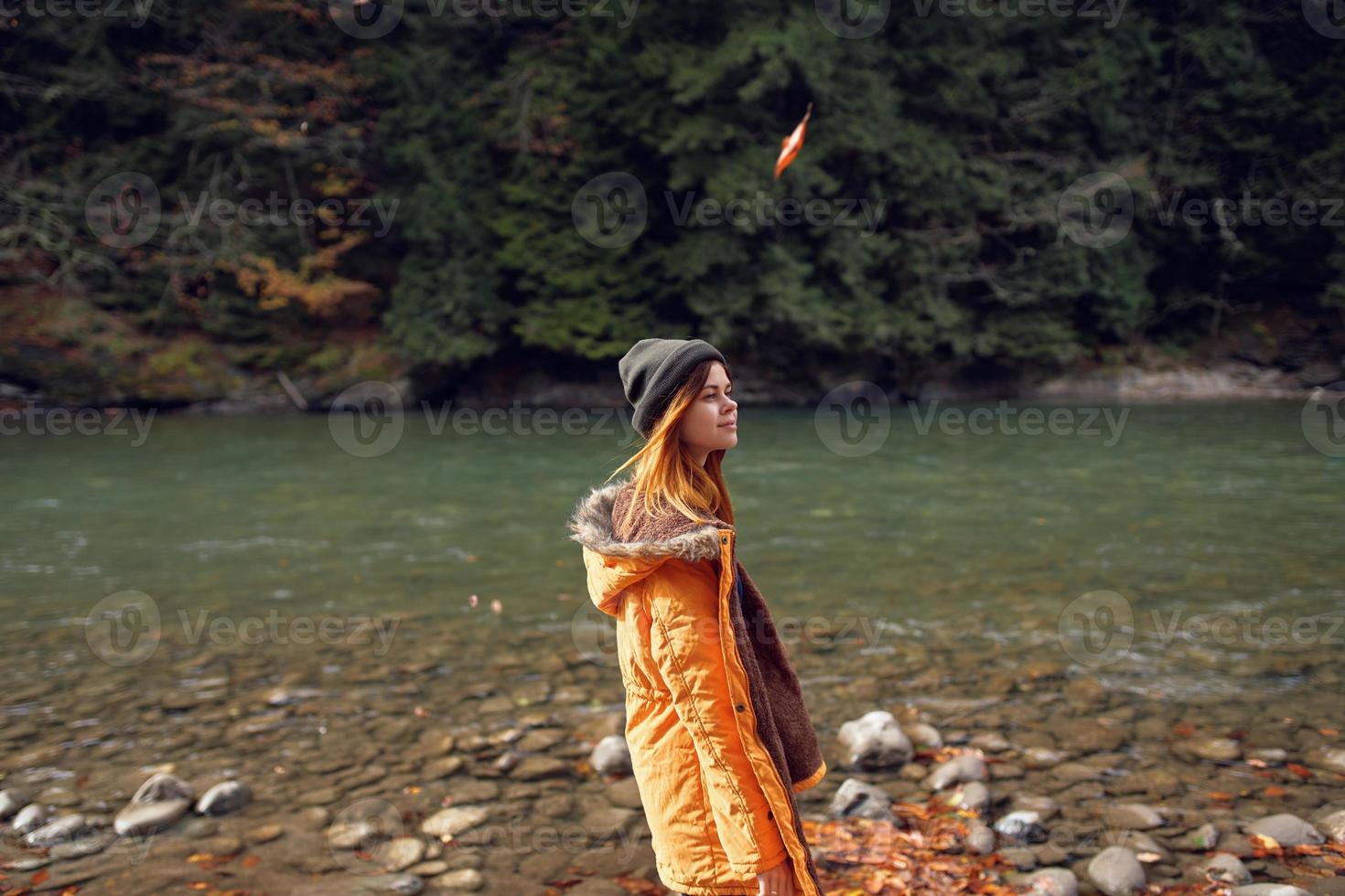 mujer en un amarillo chaqueta cerca el río admira naturaleza otoño bosque foto