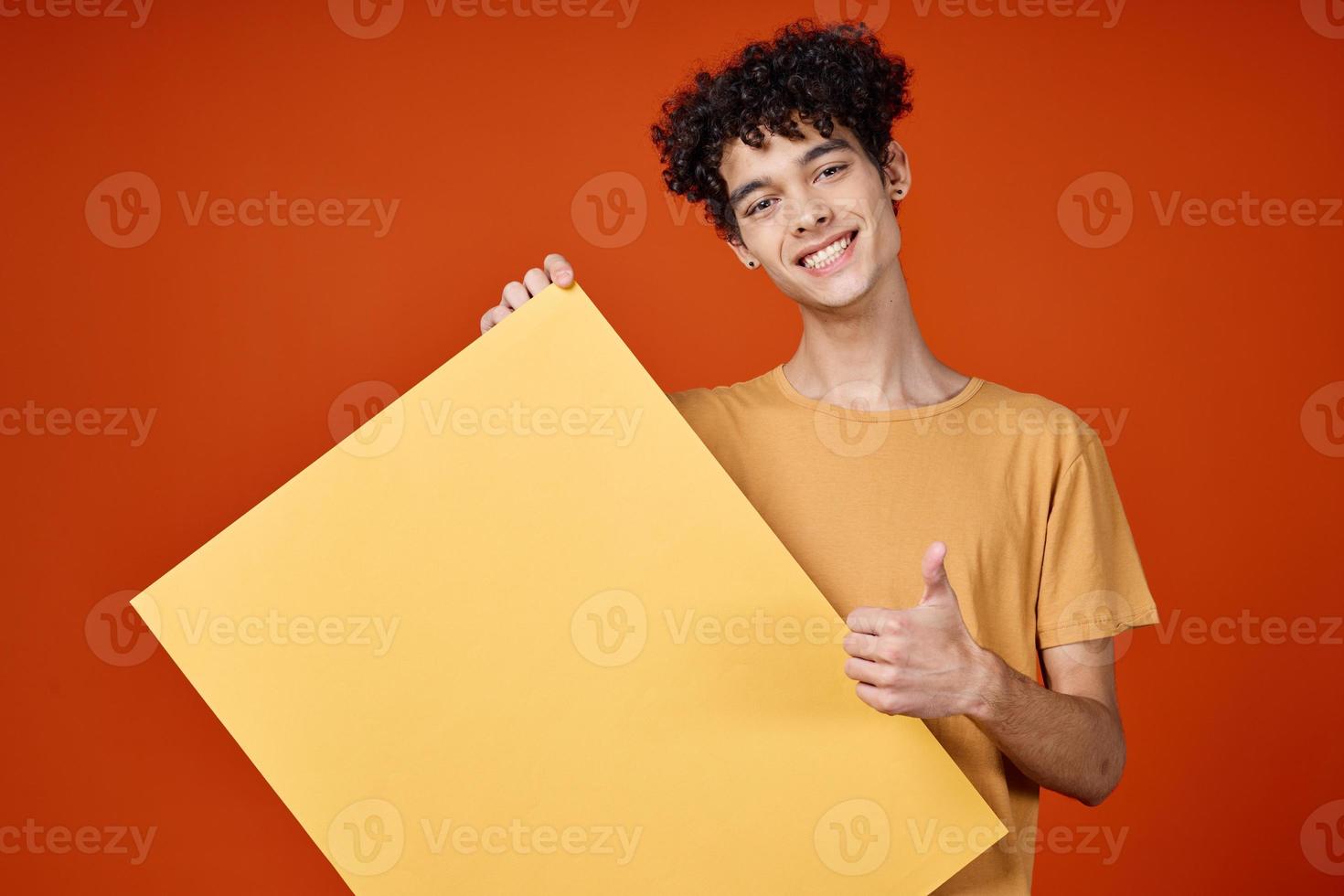 Cheerful guy with curly hair yellow poster in hands studio advertising photo