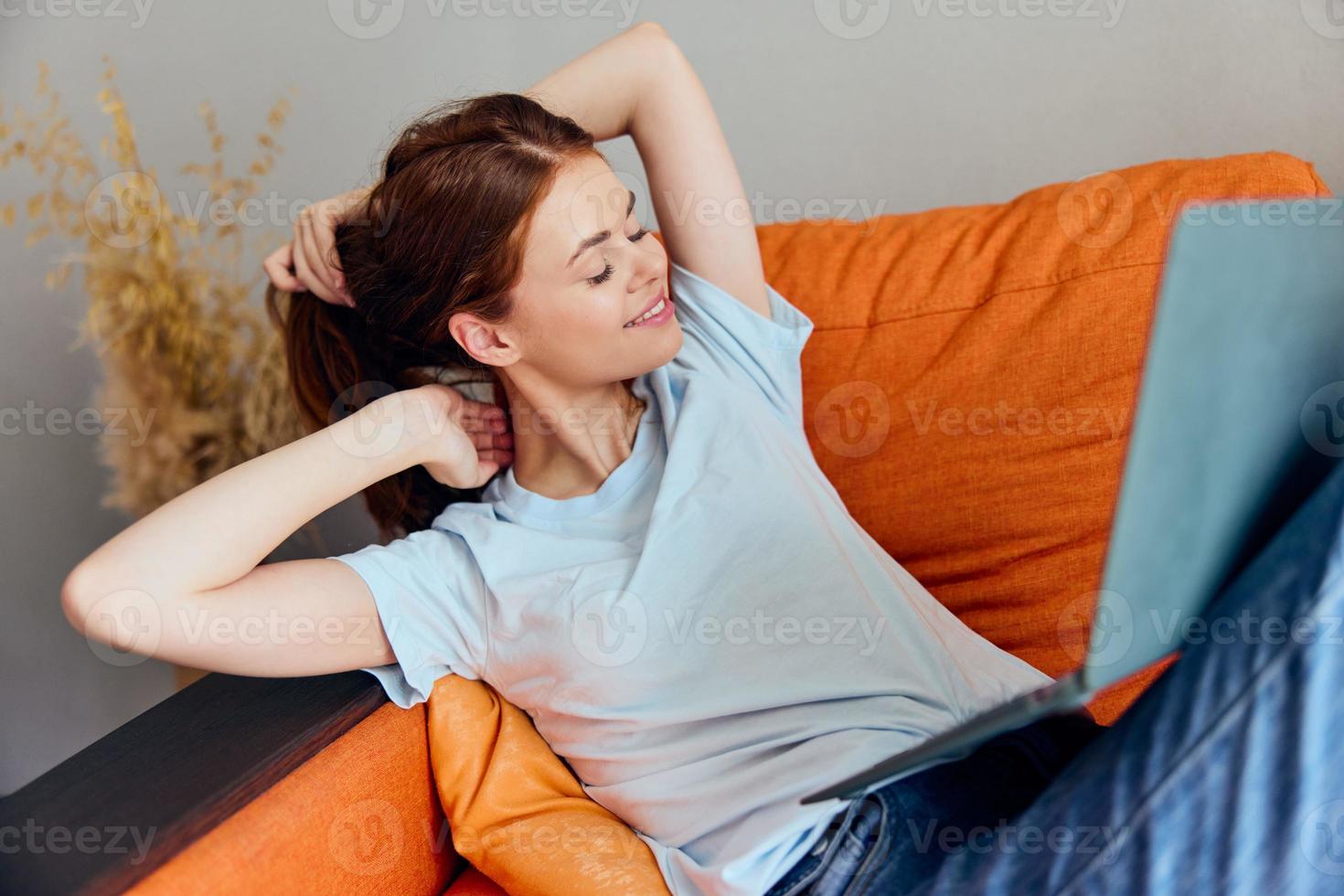 retrato de un mujer chateando en el naranja sofá con un ordenador portátil tecnologías foto