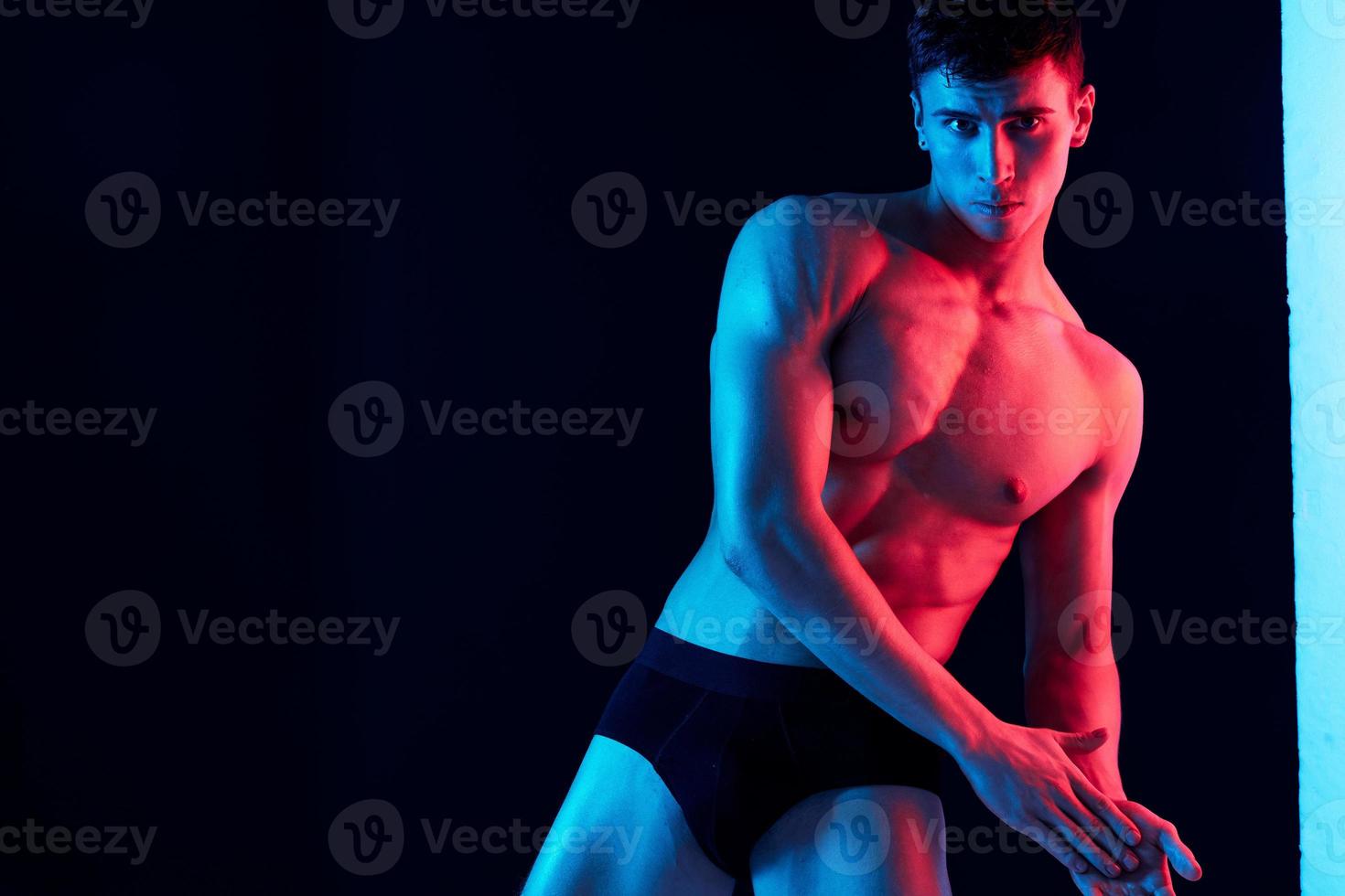 a man with an athletic physique leaned to the side and neon light black background Copy Space photo