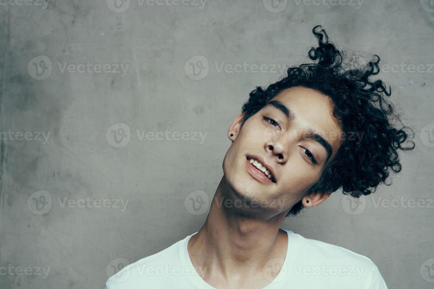 Cheerful guy with curly hair tilts his head to the side on a gray background photostudio model photo