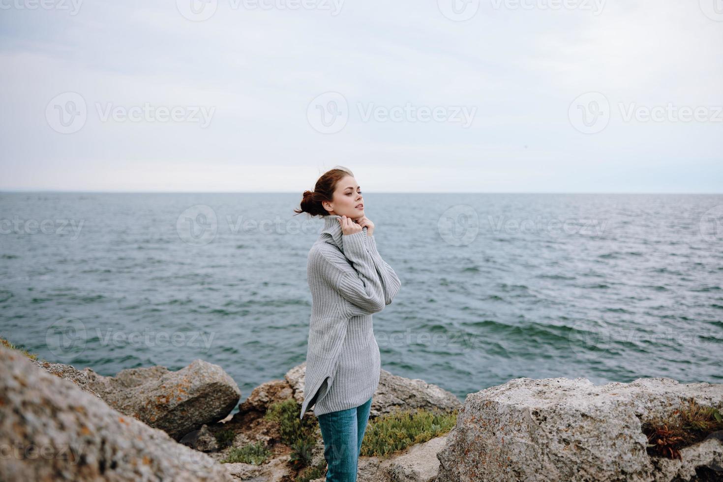 pretty woman in a gray sweater stands on a rocky shore nature female relaxing photo