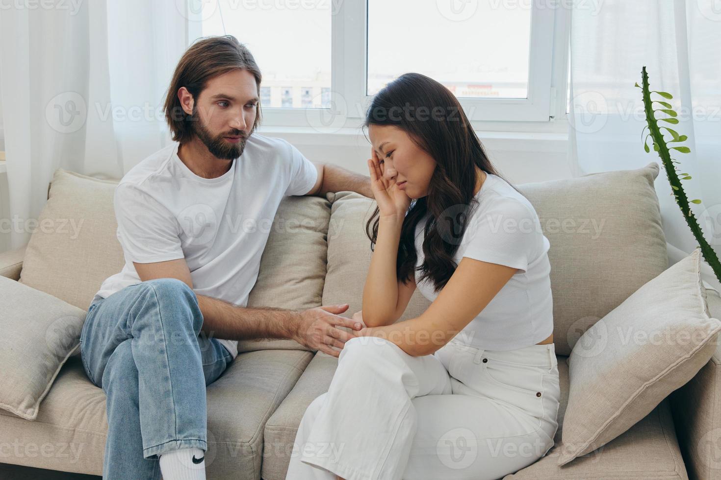 un hombre y un mujer de diferente Razas sentar en el sofá en un habitación a hogar y hablar acerca de su problemas a cada otro. un libre de estrés estilo de vida de familia peleas con psicológico apoyo foto