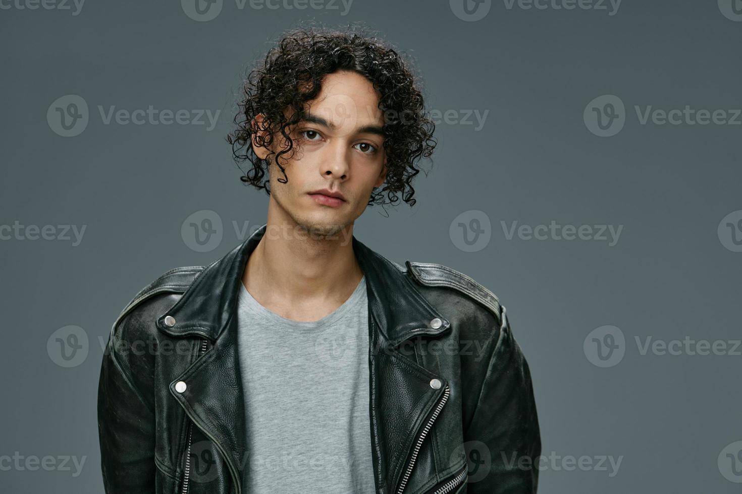 Pretty sexy self-confident stylish tanned curly man leather jacket posing isolated on over gray studio background. Cool fashion offer. Huge Seasonal Sale New Collection concept. Copy space for ad photo