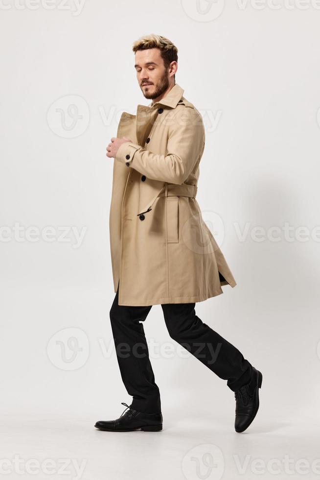 a man in a beige coat and trousers runs to the side on a light background in full growth photo