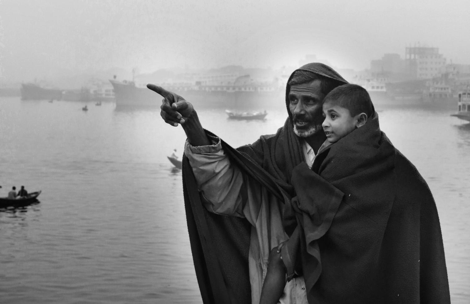 Bangladesh enero 06, 2014 un chico y su padre acecho el invierno río con el lleno cuerpo de vistiendo un grueso cobija en un invierno Mañana. foto