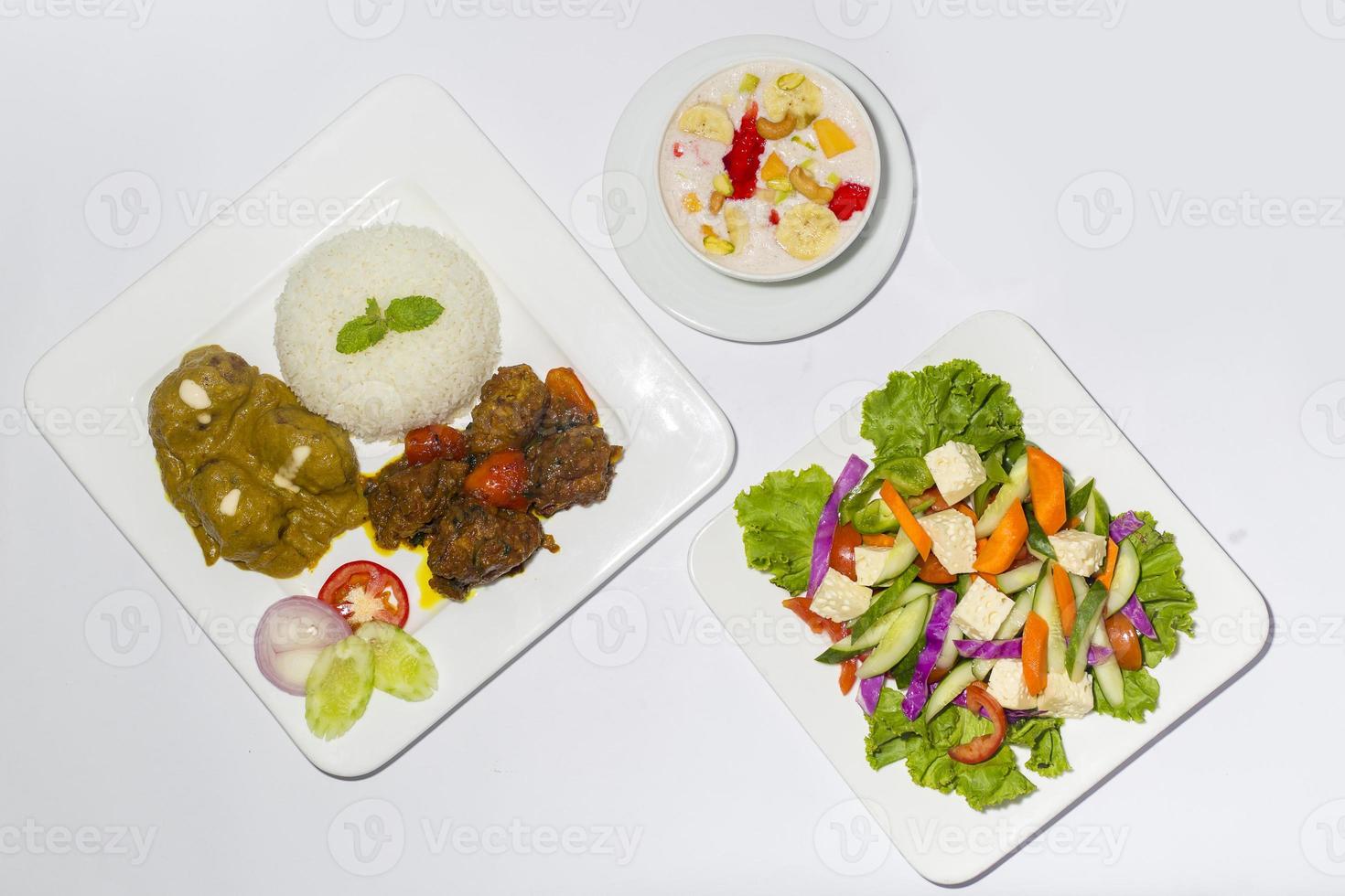 asiático estilo Ramadán sehri comida colocar. sano lleno curso comida. un plato de verde ensalada, un plato de avión arroz y 2 tipo de carne de vaca curry con faluda postre en blanco antecedentes. foto