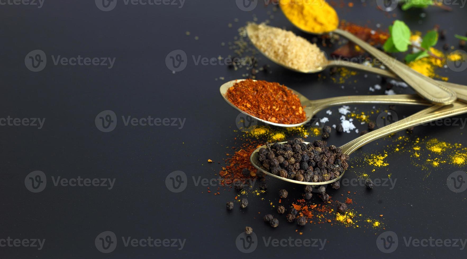 Close up dry black pepper on golden spoon against other herbs photo