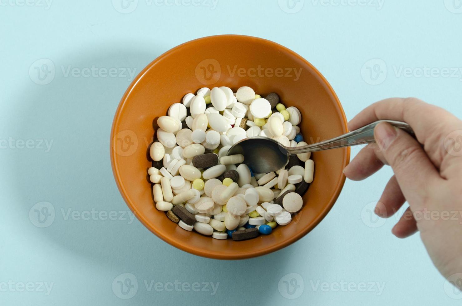 A hand scoops up medicine from a bowl. Medication with a spoon. Plate with medicines on a blue background. photo