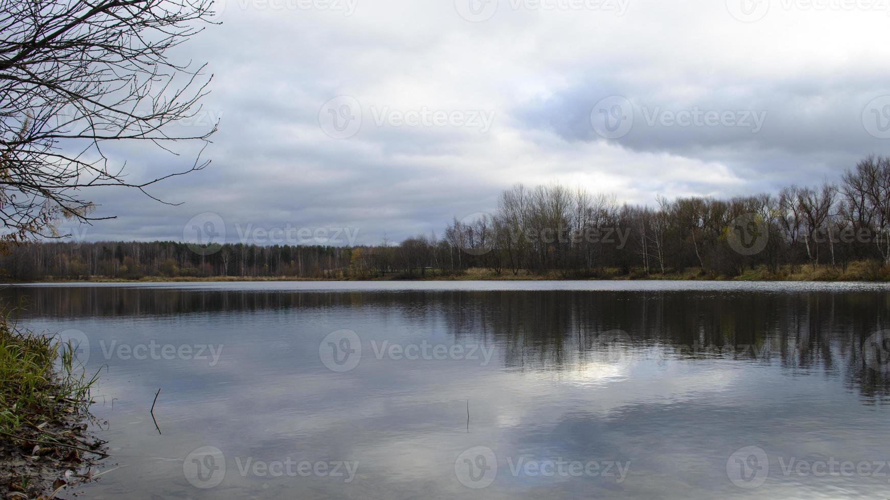 Scenic landscape. Forest around the lake. Ripples on water. Stormy weather. Stormy clouds. Sky, sunlight and trees reflecting on water. photo