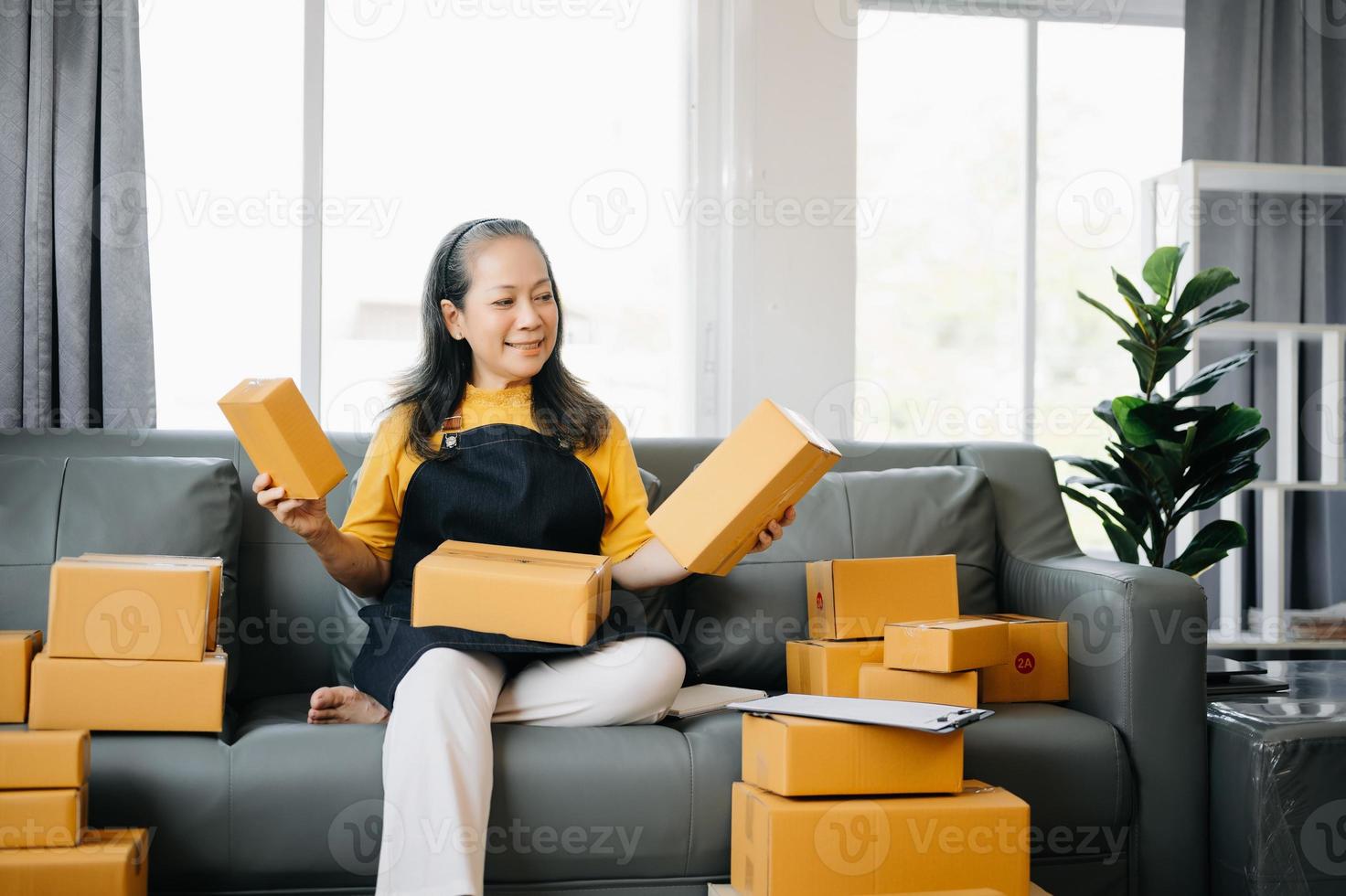 Startup small business SME, Entrepreneur owner Senior woman using smartphone or tablet taking receive and checking online purchase shopping order to preparing pack product box. photo