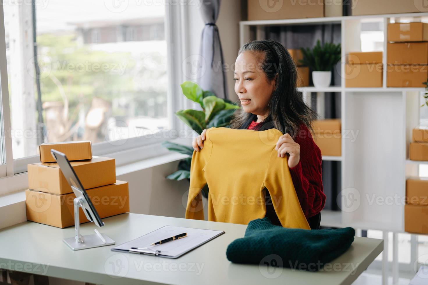 Moda blogger concepto, mayor asiático mujer de venta ropa en vídeo streaming.startup pequeño negocio pequeño, utilizando teléfono inteligente o tableta tomando recibir y comprobación foto