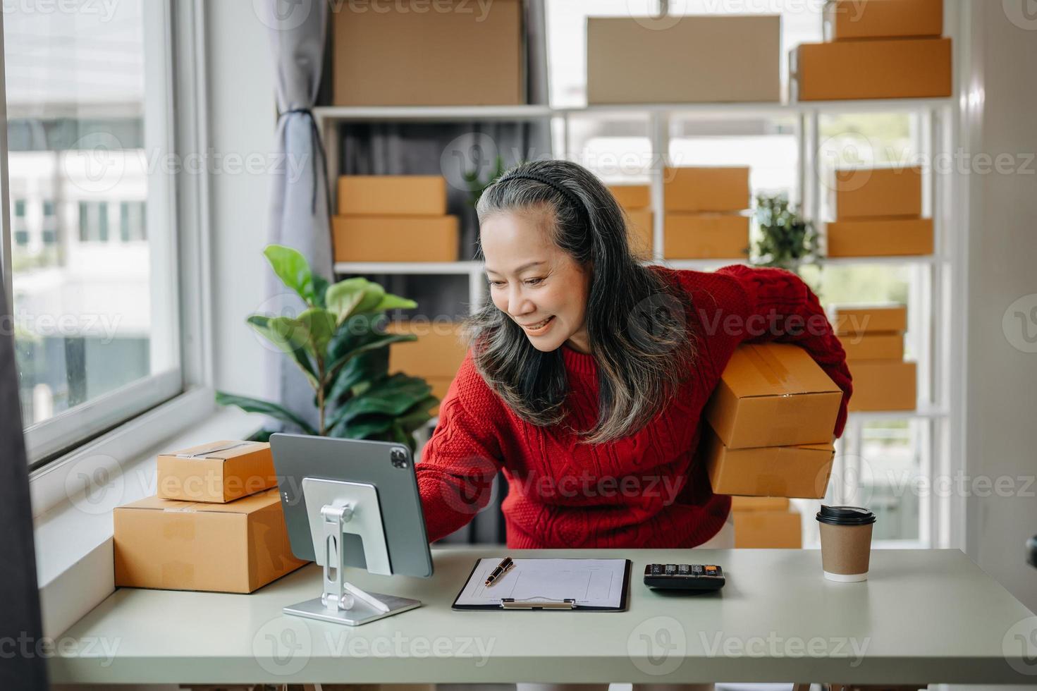 Senior business owner woman prepare parcel box and standing check online orders for deliver to customer on tablet, laptop Shopping Online concept. at home office photo