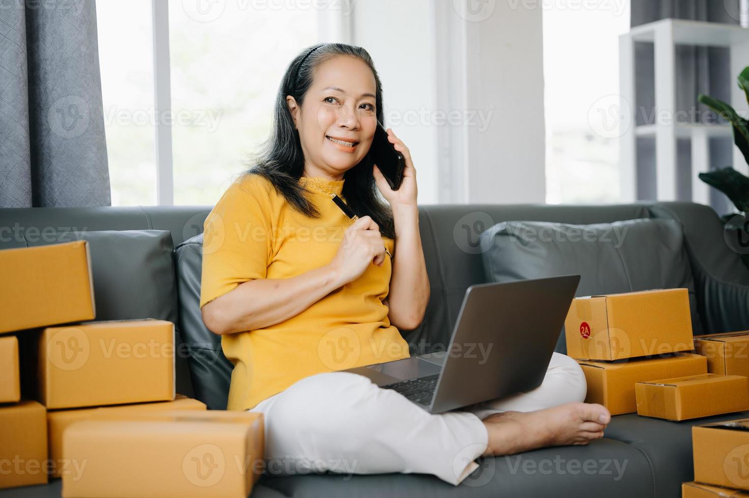 mayor negocio propietario mujer preparar paquete o empaquetar caja y en pie cheque en línea pedidos para entregar a cliente en tableta, ordenador portátil compras en línea concepto. foto