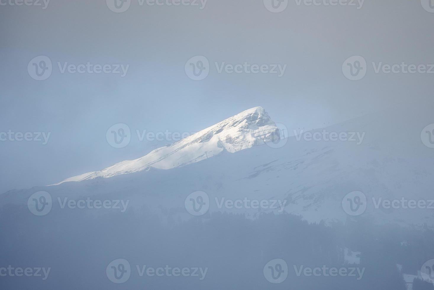 Scenic view of snow covered mountain peak seen through fog photo