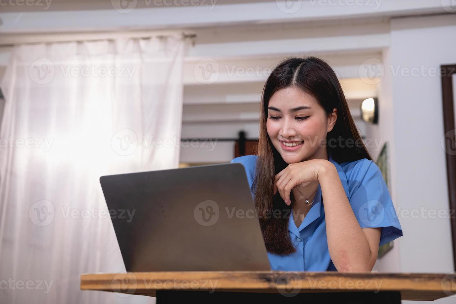 Asian woman with a beautiful smile and face sits comfortably on her desk at home with a laptop and notebook for relaxing and relaxing in a bright morning. holiday vacation concept. photo