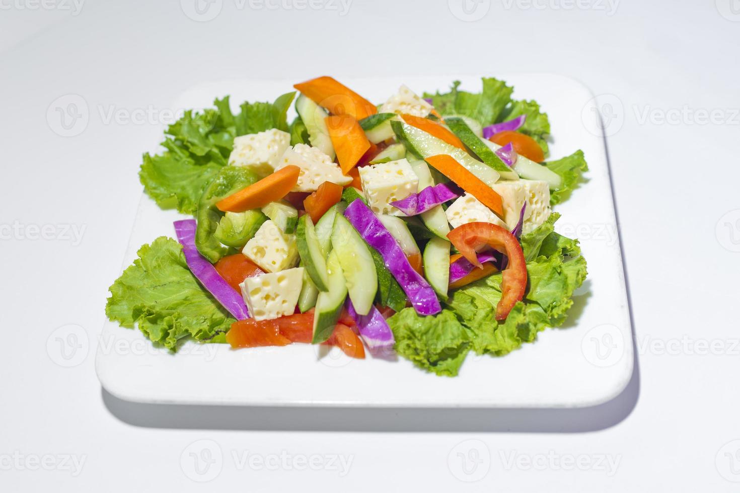 Fresh green vegetable salad in a plate. Healthy capsicume, carrot, cheese, tomato and lettuce meal on white background photo