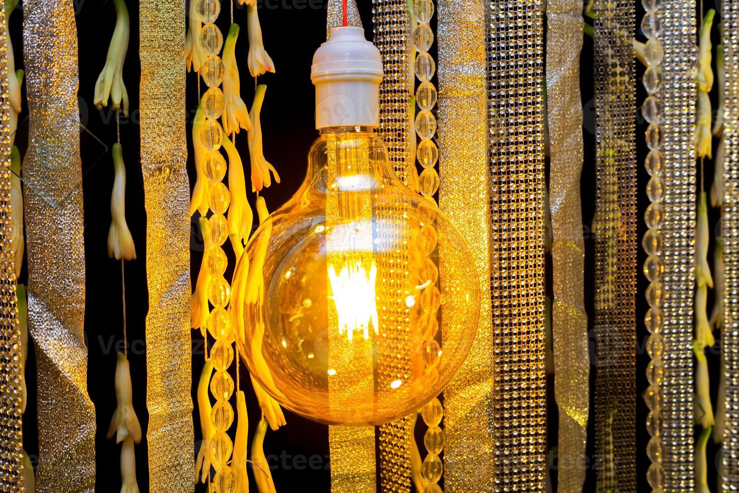 Colorful artificial flowers with Decorative antique Edison style filament light bulbs hanging on wedding stage decoration. photo