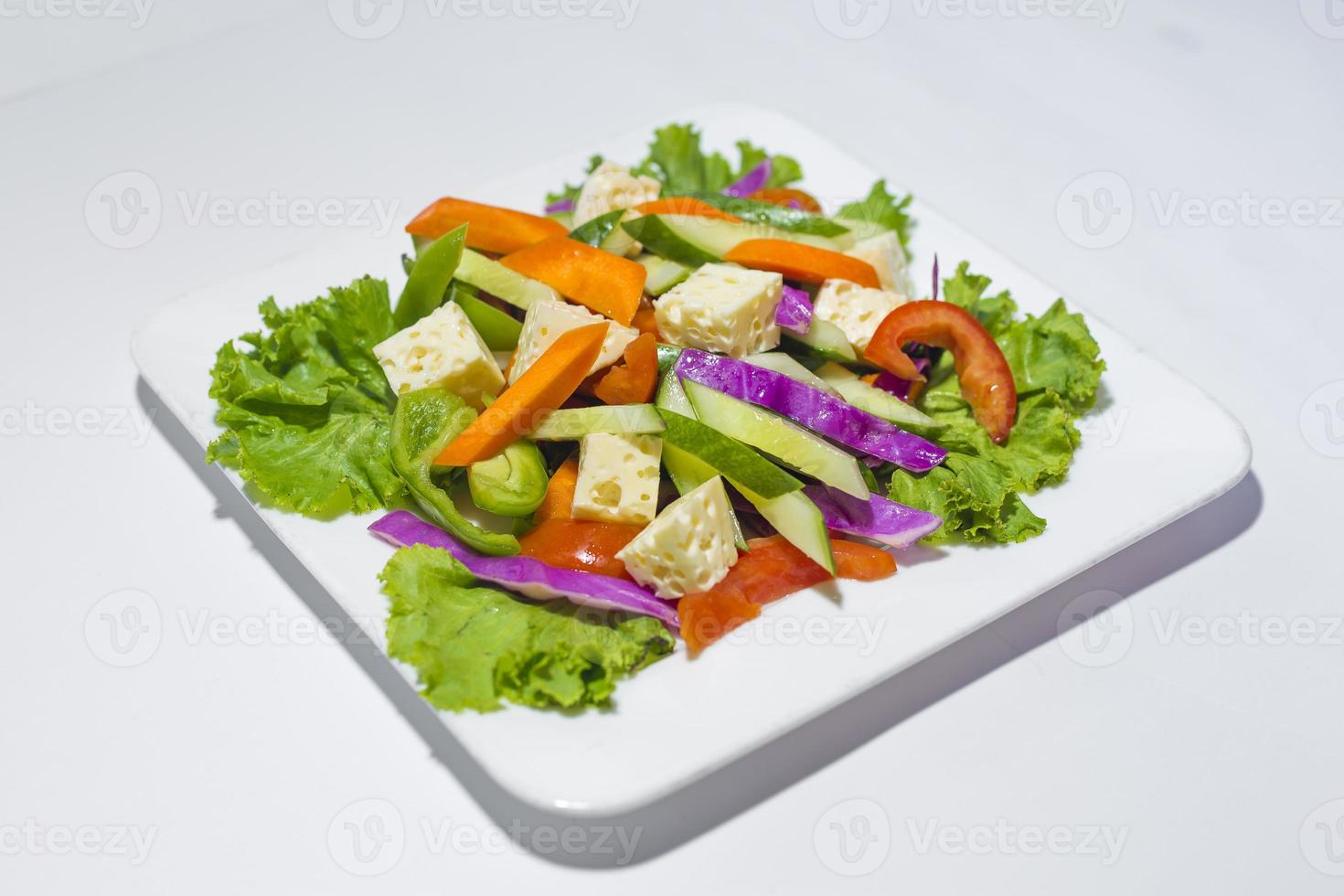 Fresh green vegetable salad in a plate. Healthy capsicume, carrot, cheese, tomato and lettuce meal on white background photo