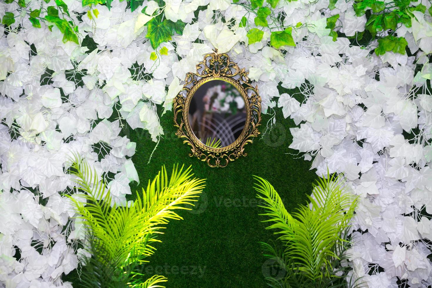 Green artificial grass based wedding stage with handcrafted oval-shaped vanity wall mirror decoration background. Plastic artificial flower. Wedding decoration. photo