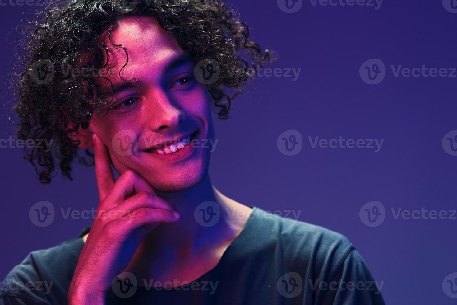 Cute stylish happy cheerful curly man in black t-shirt posing isolated on color pink blue studio background. Cool fashion offer. Virtual Reality New Collection concept. Copy space for ad photo