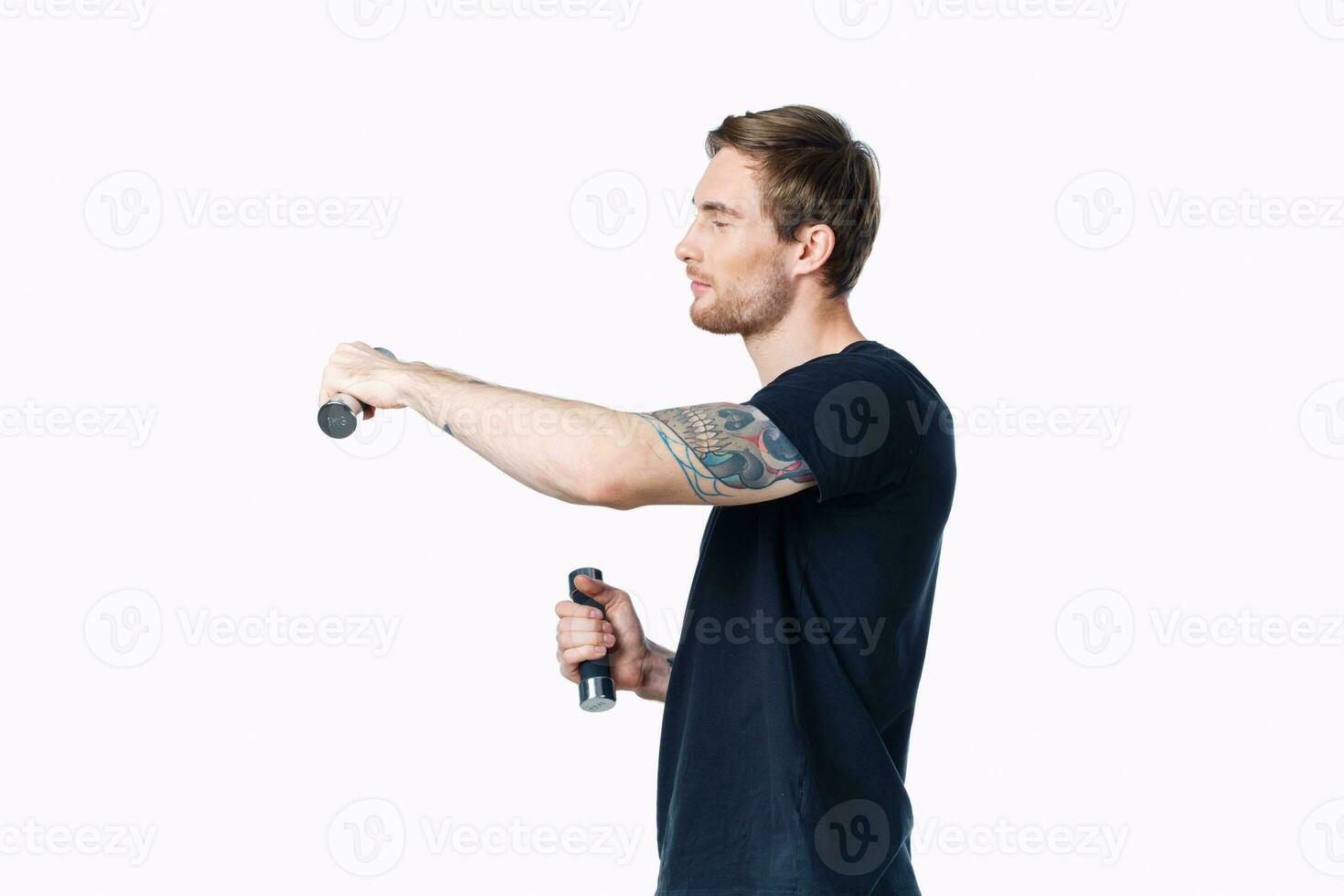 athlete in a black t-shirt are engaged in fitness on a white background indoors and dumbbells in hand photo