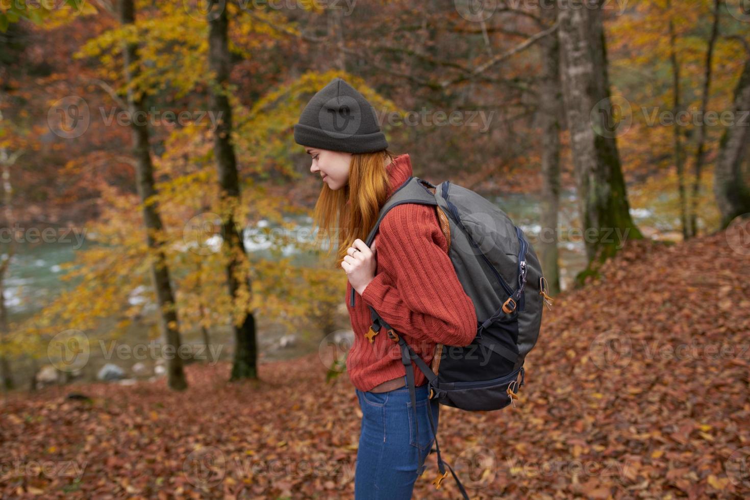 woman with backpack walking in the autumn park near the river in nature side view photo