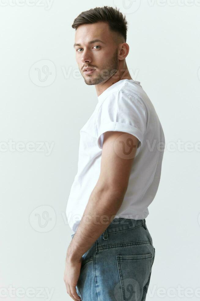 View from the back shot of handsome serious tanned man guy in basic t-shirt looks at camera posing on white background. Fashion Style New Collection Offer. Copy space for ad. Model snap photo