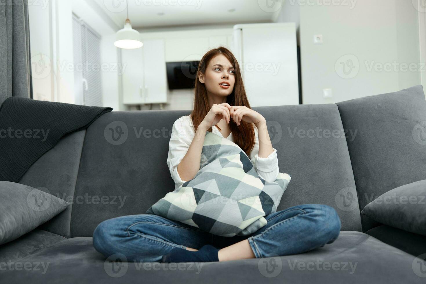 un mujer en un Departamento se sienta en un sofá con un almohada en su manos comodidad foto