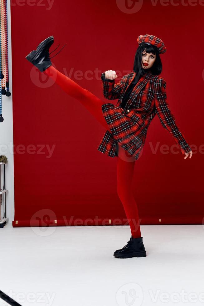 stylish woman in a bright suit lifted her leg up on a red background photo