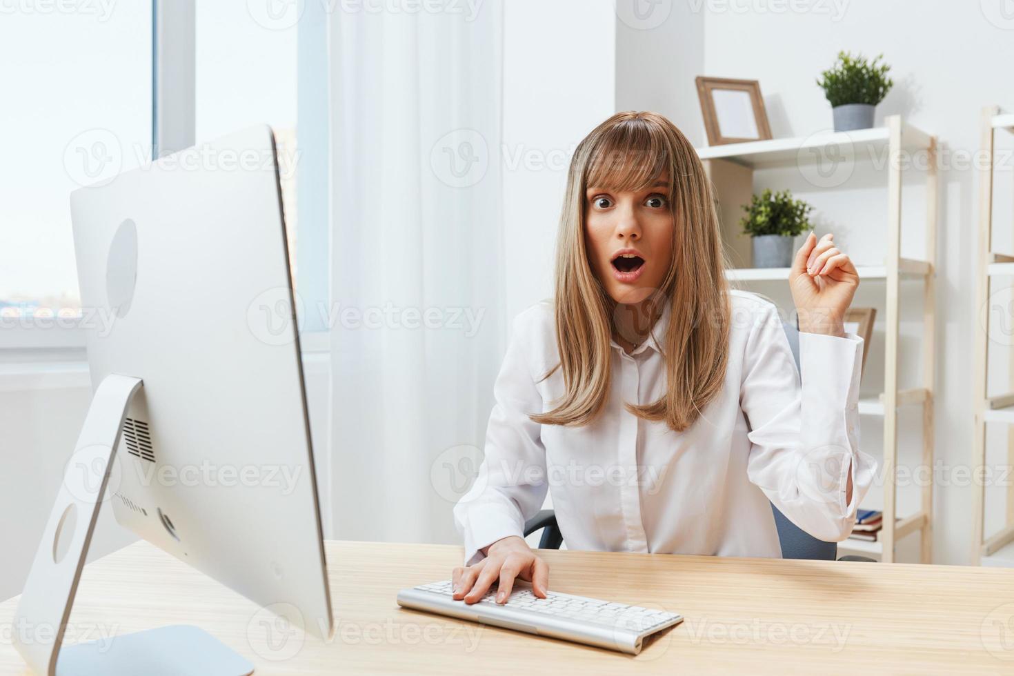 Shocked excited pretty blonde businesswoman freelancer look at camera open mouth point finger up have insight in light modern office. Employee work on computer online making decision. Copy space photo