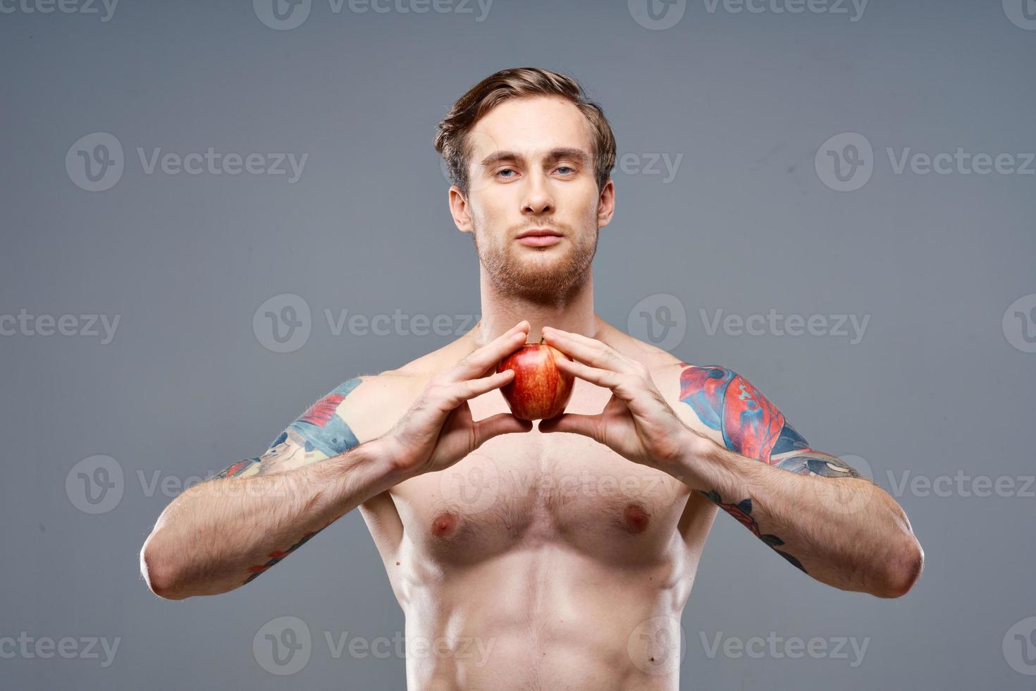 male athlete with an apple in his hands and tattoo cubes on his stomach biceps press photo