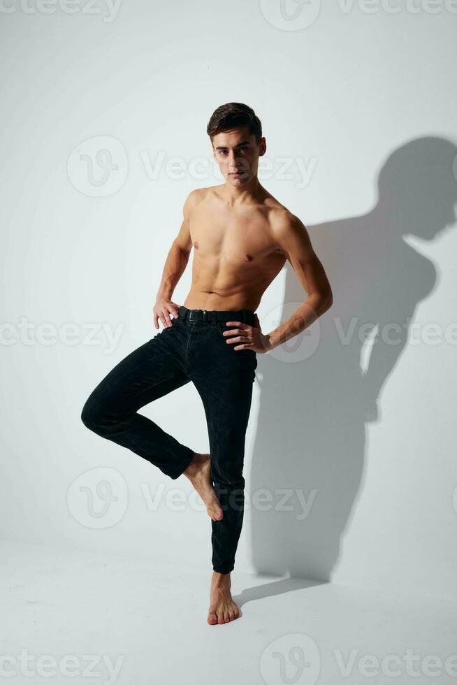 A man in trousers and a naked torso stands on one leg against a light background photo