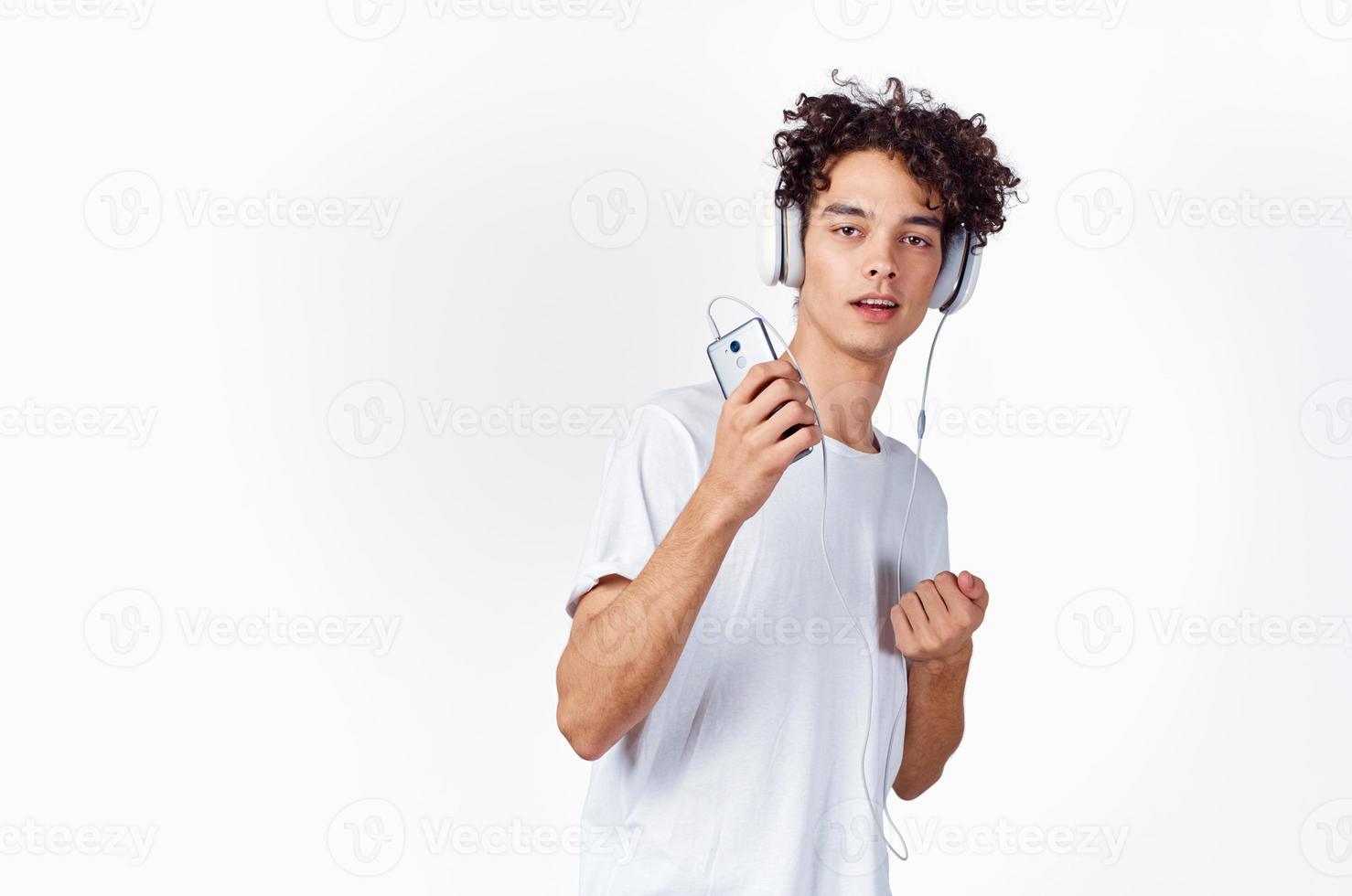 gracioso chico con Rizado pelo en un blanco camiseta escucha a música tecnología entretenimiento foto