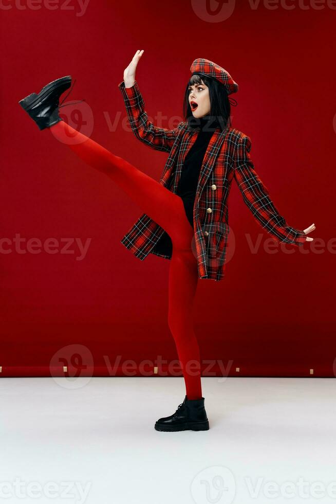 brunette in a plaid coat in red leggings and a hat lifted her leg up photo