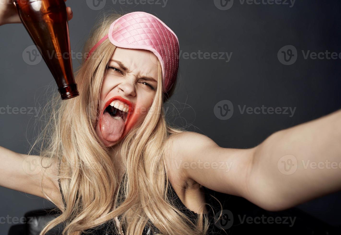 Drunk woman with a bottle of beer on a gray background gestures with her hands and bright makeup photo