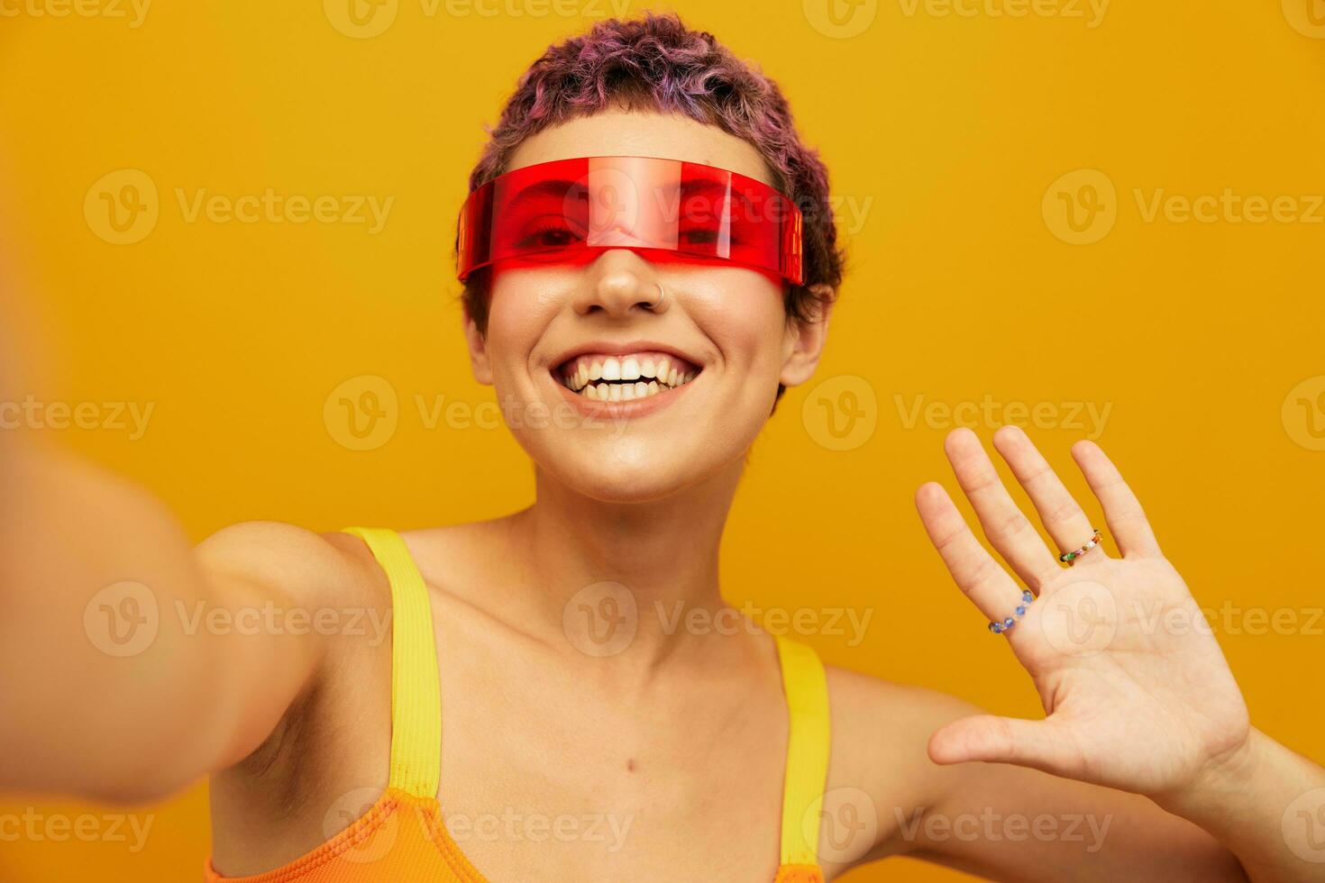 Woman wearing unusual millennial glasses taking selfies in sportswear against an orange studio background, free space photo