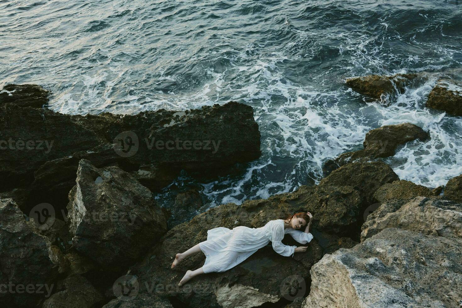 Barefoot woman in a secluded spot on a wild rocky coast in a white dress vacation concept photo
