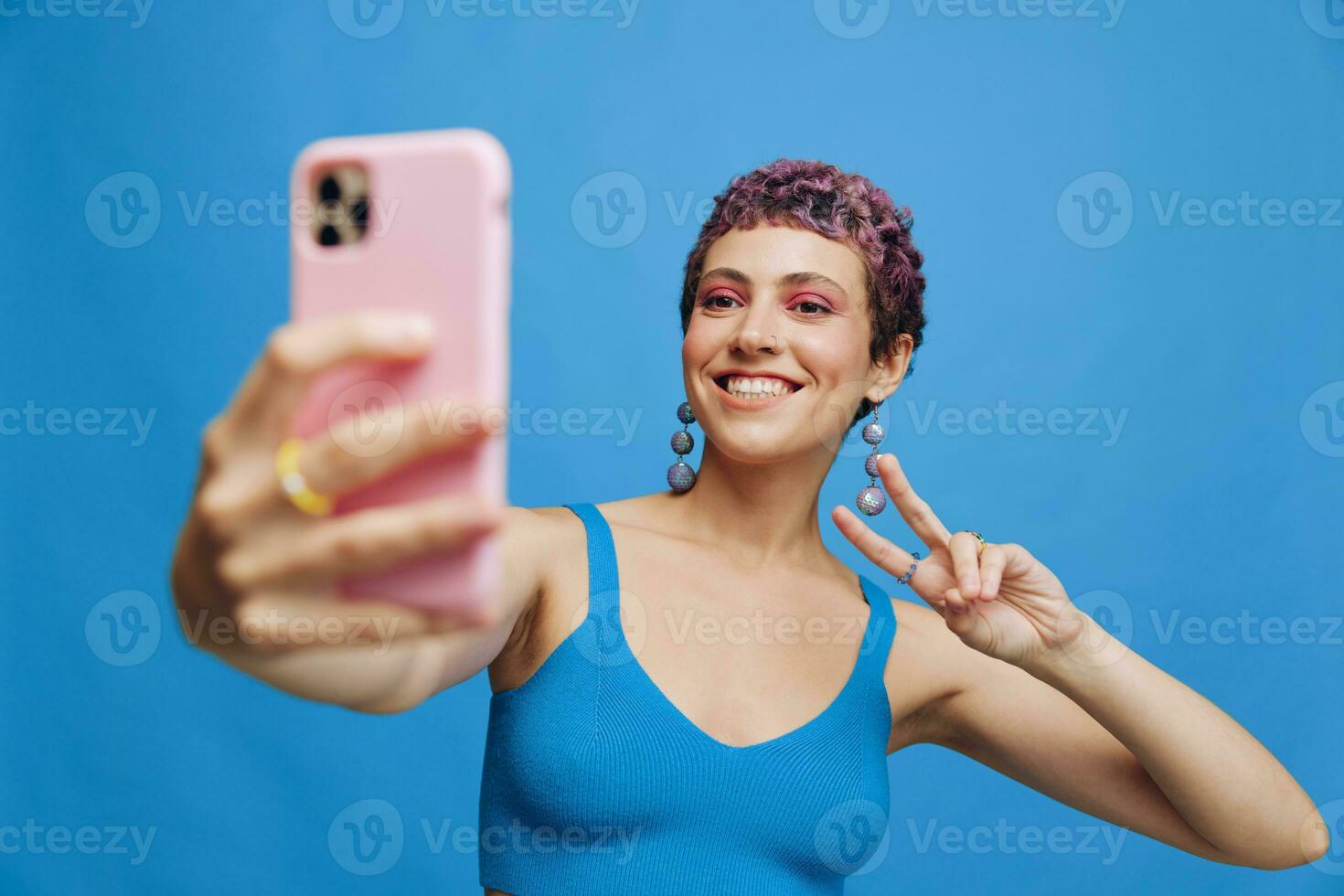 Young sports woman fashion blogger takes a picture of herself on the phone in blue sportswear smiling and showing her tongue on a blue monochrome background photo